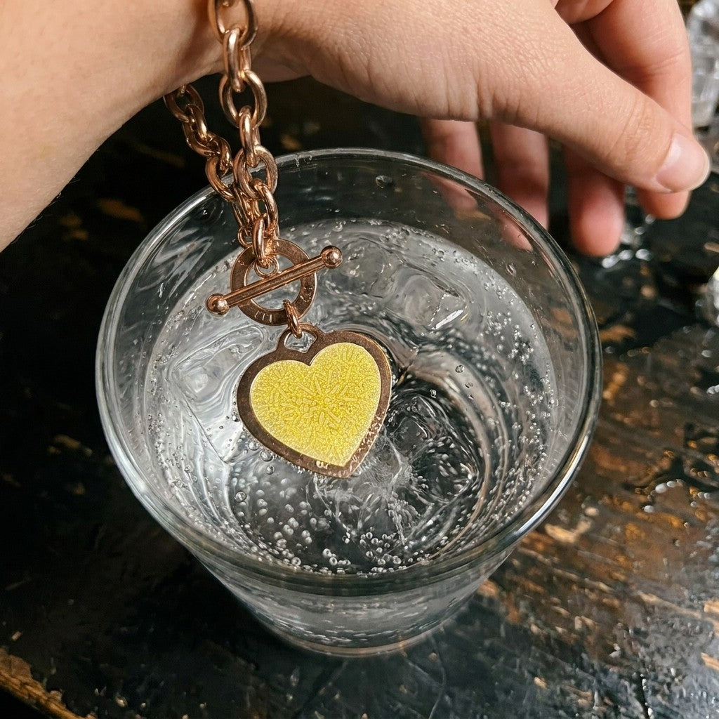 The No Lace charm bracelet's heart tag with a yellow test sticker dipped into a sparkling drink