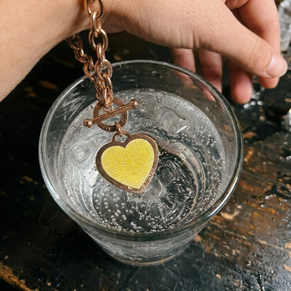 The No Lace charm bracelet's heart tag with a yellow test sticker dipped into a sparkling drink